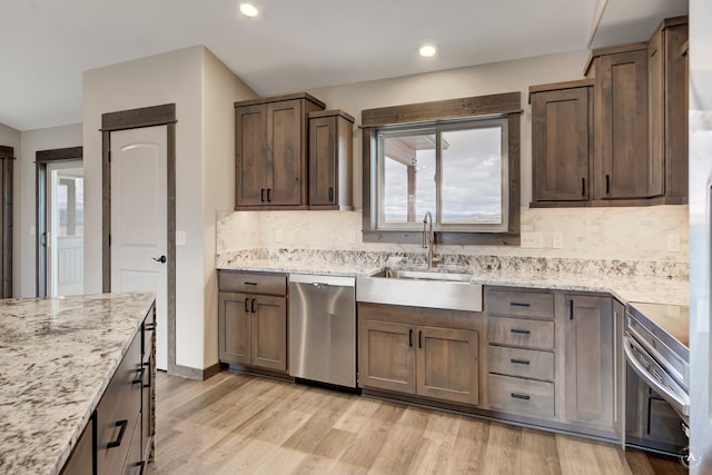 kitchen featuring sink, light stone counters, backsplash, light hardwood / wood-style floors, and appliances with stainless steel finishes