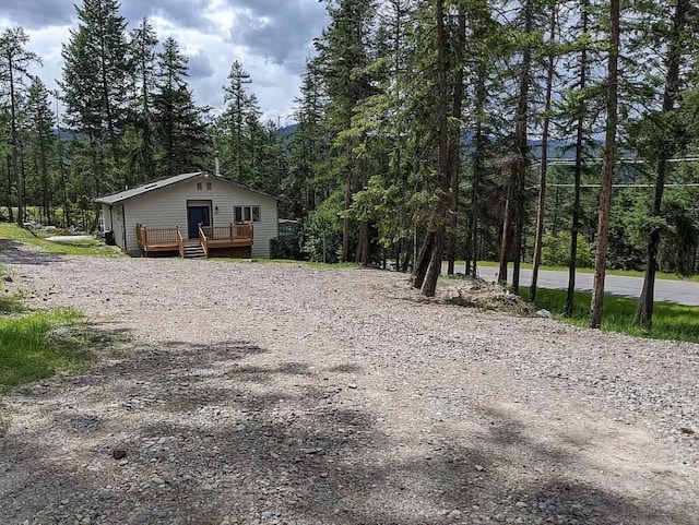 exterior space featuring driveway, a wooden deck, and a view of trees