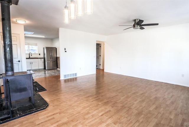 living room featuring light wood-type flooring, a wood stove, visible vents, and ceiling fan