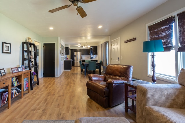 living room with light hardwood / wood-style floors and ceiling fan with notable chandelier