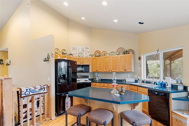 kitchen with a kitchen breakfast bar, sink, black appliances, a center island, and light hardwood / wood-style floors