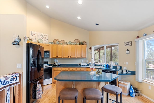 kitchen featuring a kitchen bar, a wealth of natural light, black appliances, and light hardwood / wood-style floors