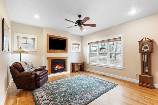 living room featuring ceiling fan, a textured ceiling, and light wood-type flooring