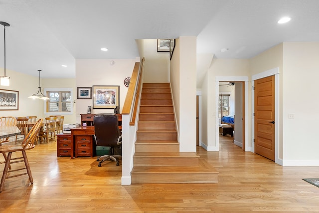 stairs featuring a healthy amount of sunlight, ceiling fan with notable chandelier, and hardwood / wood-style floors