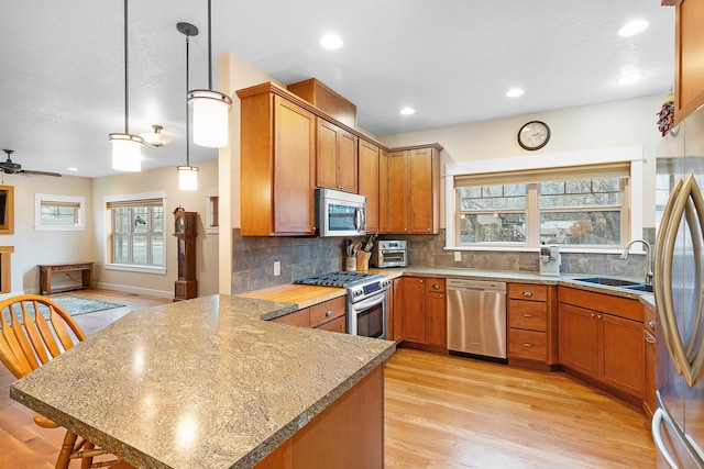 kitchen featuring pendant lighting, stainless steel appliances, sink, kitchen peninsula, and ceiling fan