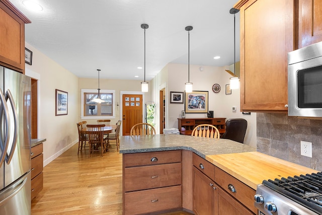 kitchen featuring pendant lighting, decorative backsplash, kitchen peninsula, light wood-type flooring, and stainless steel appliances