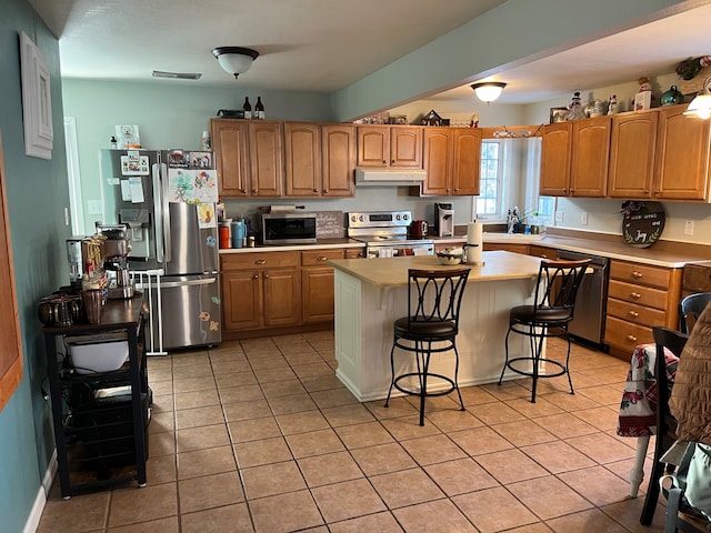 kitchen with a kitchen breakfast bar, a kitchen island, light tile patterned flooring, and stainless steel appliances