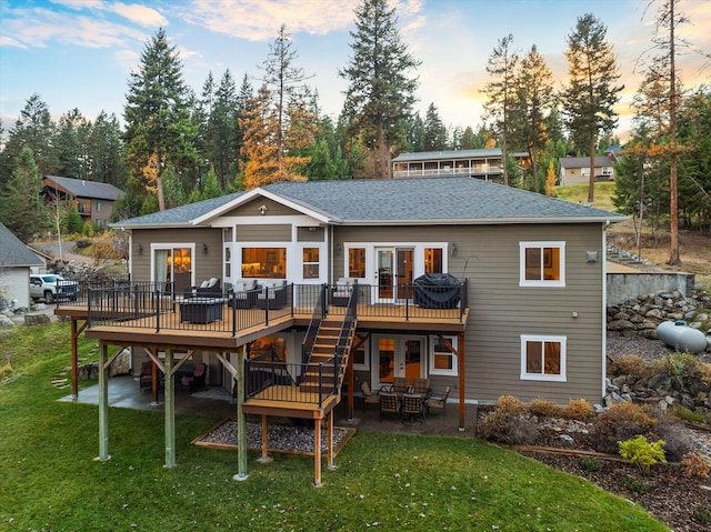 back house at dusk with a lawn, a patio, and a wooden deck