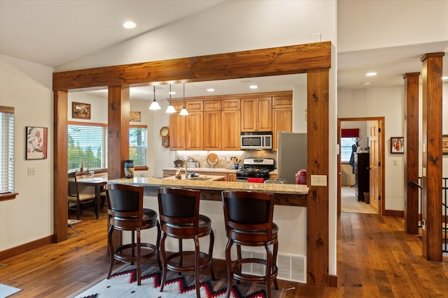 kitchen with dark wood-type flooring, sink, vaulted ceiling, light stone counters, and stainless steel appliances