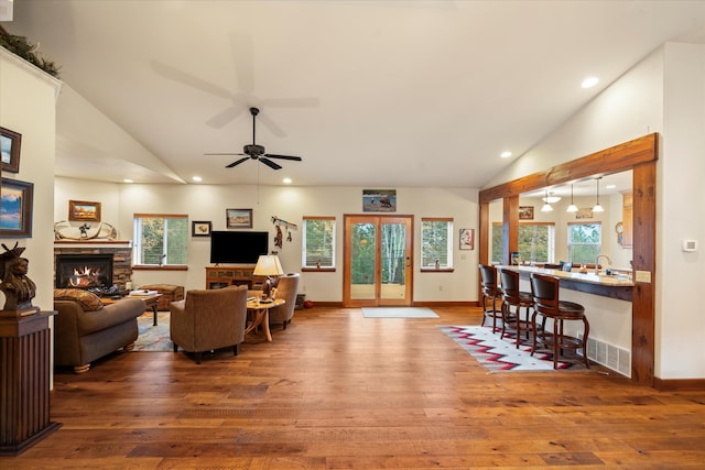 living room featuring high vaulted ceiling, a stone fireplace, sink, ceiling fan, and wood-type flooring