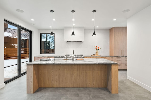 kitchen featuring light stone countertops, an island with sink, and hanging light fixtures