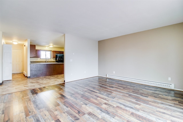 unfurnished living room featuring baseboard heating, sink, and light wood-type flooring