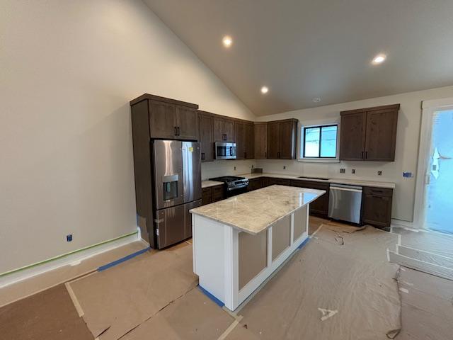 kitchen featuring dark brown cabinetry, a center island, high vaulted ceiling, stainless steel appliances, and light stone countertops