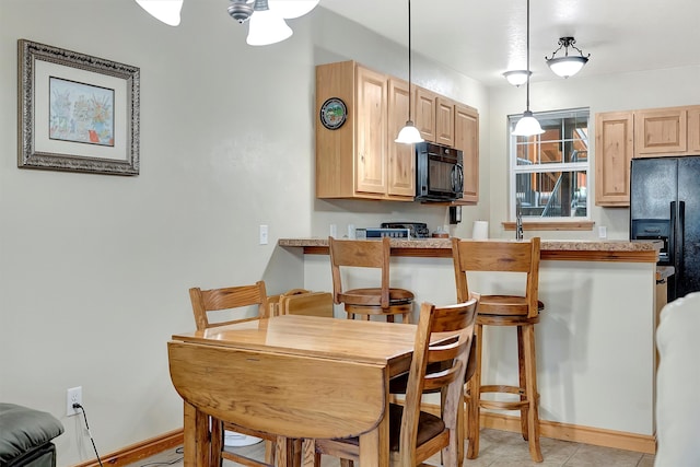 kitchen featuring black appliances, kitchen peninsula, hanging light fixtures, and light brown cabinetry