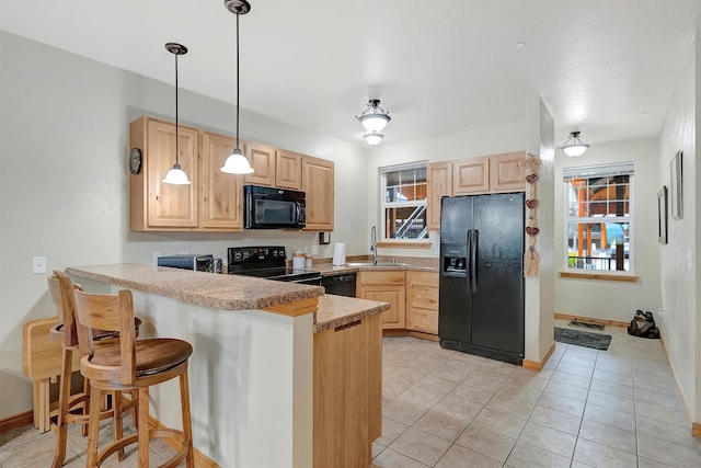 kitchen with kitchen peninsula, a kitchen bar, black appliances, light brown cabinets, and hanging light fixtures