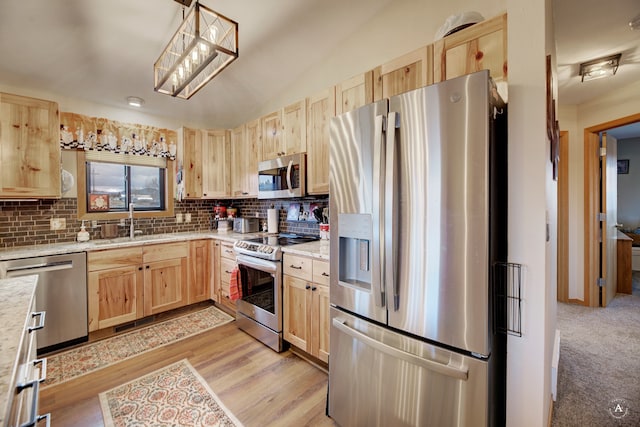 kitchen featuring light brown cabinets, hanging light fixtures, light wood-type flooring, appliances with stainless steel finishes, and tasteful backsplash