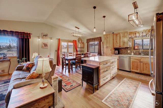 kitchen featuring appliances with stainless steel finishes, light wood-type flooring, tasteful backsplash, light brown cabinets, and a kitchen island