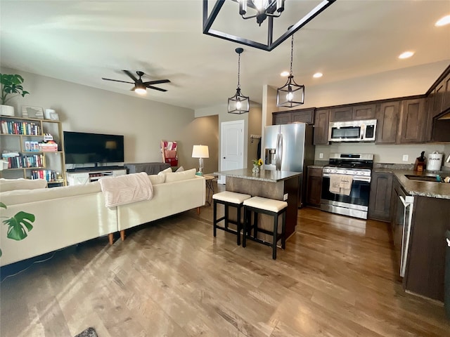 kitchen with appliances with stainless steel finishes, dark brown cabinets, hardwood / wood-style floors, a center island, and a breakfast bar area