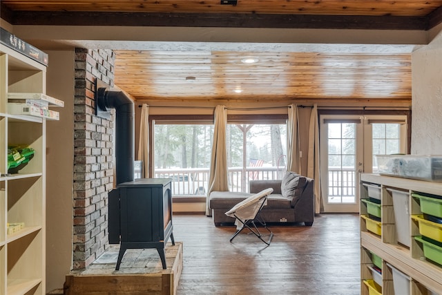 living area featuring dark wood-type flooring, a wood stove, a healthy amount of sunlight, and wood ceiling