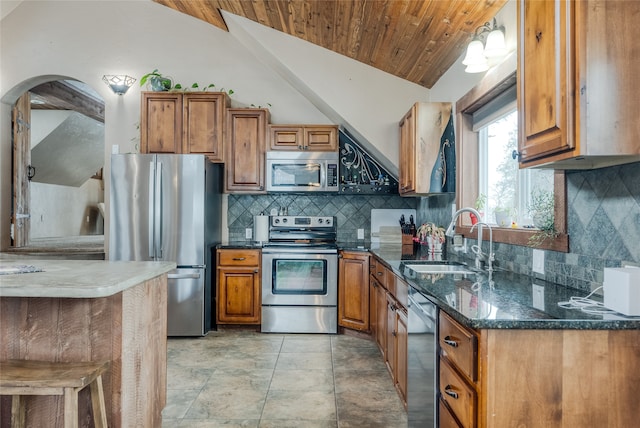 kitchen with lofted ceiling, sink, dark stone countertops, appliances with stainless steel finishes, and tasteful backsplash