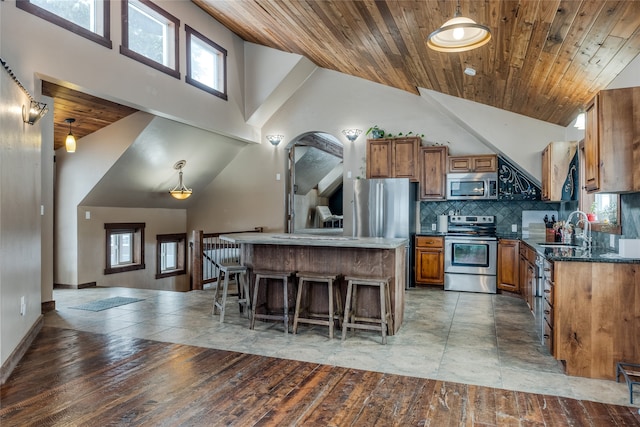 kitchen featuring decorative light fixtures, a kitchen island, stainless steel appliances, and high vaulted ceiling