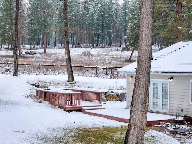 yard layered in snow with a wooden deck and french doors