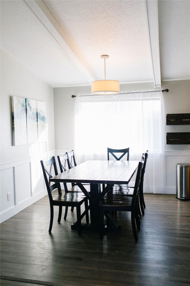 dining room with beam ceiling, a textured ceiling, dark wood finished floors, and a decorative wall