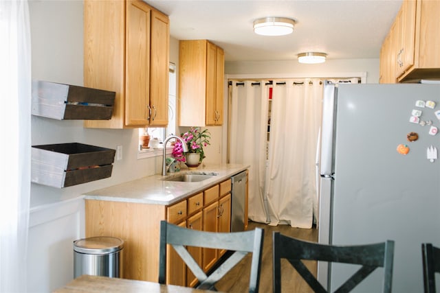 kitchen with stainless steel dishwasher, light countertops, freestanding refrigerator, and a sink