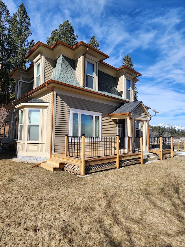 back of house with a deck, a shingled roof, and a lawn