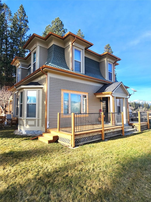 rear view of house with roof with shingles, a deck, mansard roof, and a yard