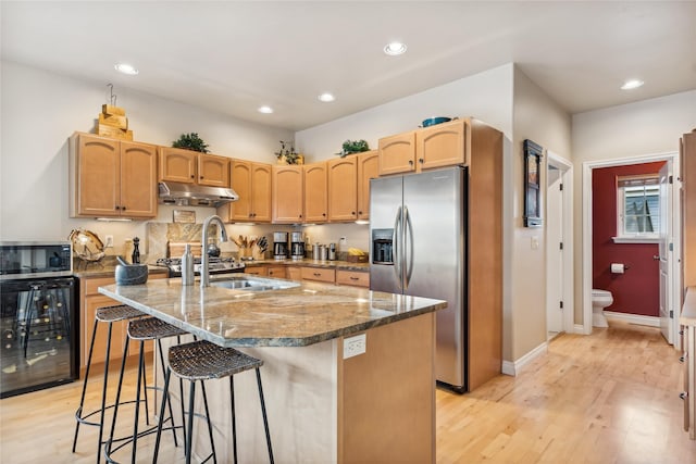 659 Copperwood Ct, Whitefish, MT 59937 - kitchen with appliances with stainless steel finishes, wine cooler, under cabinet range hood, light wood-style floors, and dark stone counters