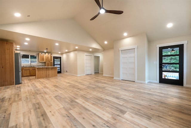 unfurnished living room with a healthy amount of sunlight, light wood-type flooring, ceiling fan, and high vaulted ceiling