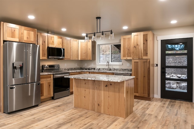 kitchen featuring light stone counters, a center island, light wood-type flooring, pendant lighting, and stainless steel appliances