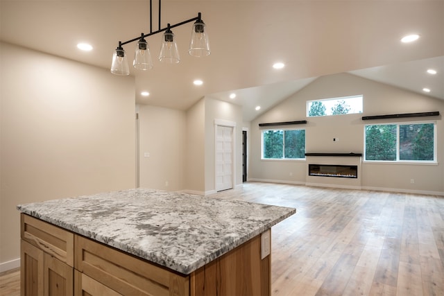 kitchen with lofted ceiling, light stone counters, decorative light fixtures, light hardwood / wood-style flooring, and a kitchen island