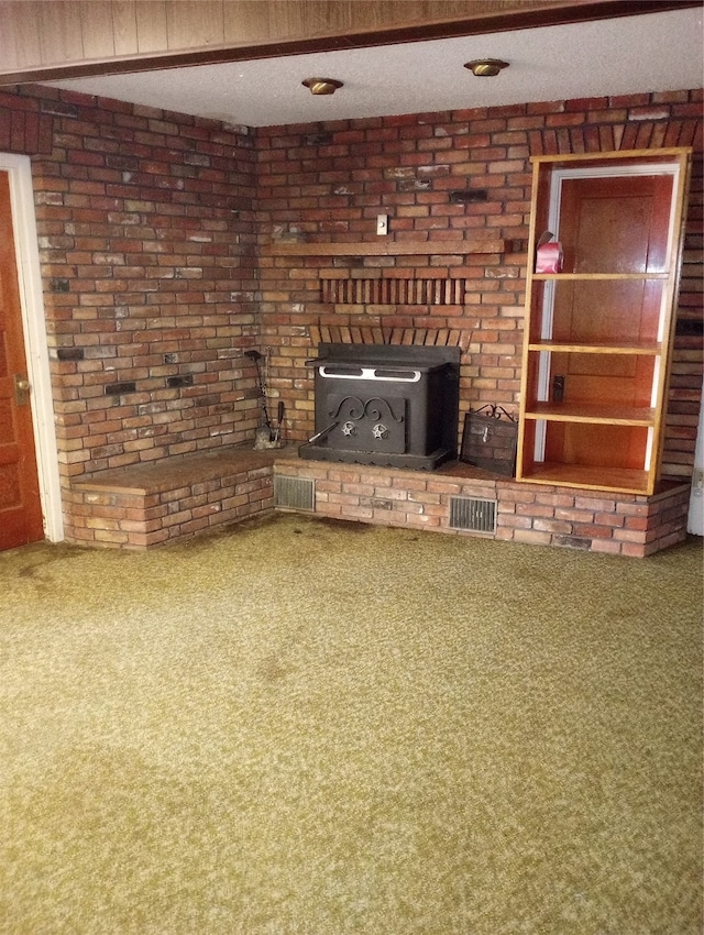 unfurnished living room featuring carpet flooring, a textured ceiling, a wood stove, and brick wall