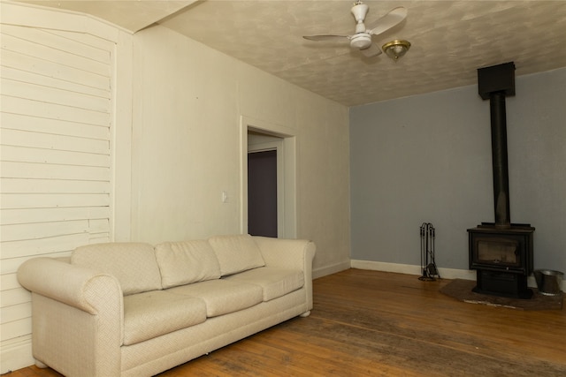 living room with hardwood / wood-style floors, a wood stove, and ceiling fan