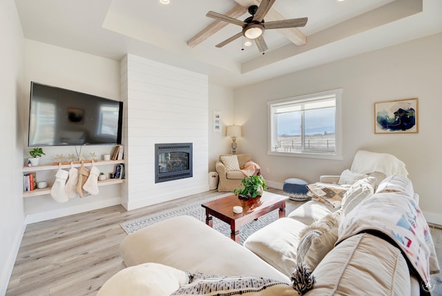 living room with ceiling fan, a large fireplace, a tray ceiling, and light wood-type flooring