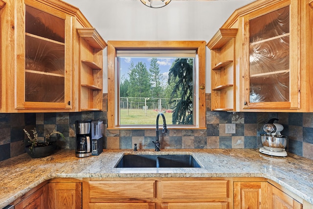 kitchen with tasteful backsplash, light stone countertops, and sink