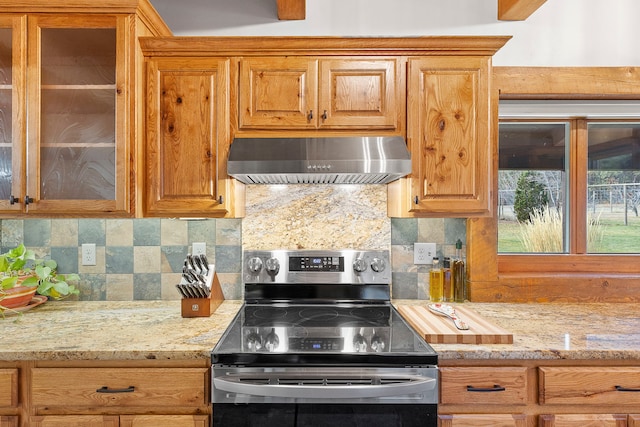 kitchen with decorative backsplash, electric range, light stone counters, and wall chimney range hood