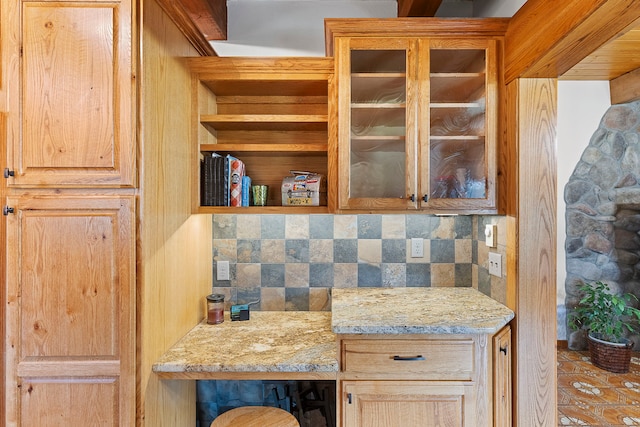 kitchen featuring light stone countertops, built in desk, light brown cabinetry, and tasteful backsplash