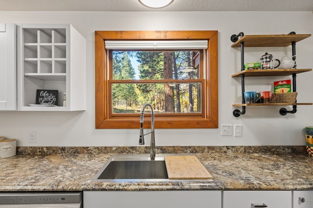 kitchen with stainless steel dishwasher, a textured ceiling, sink, dark stone countertops, and white cabinets