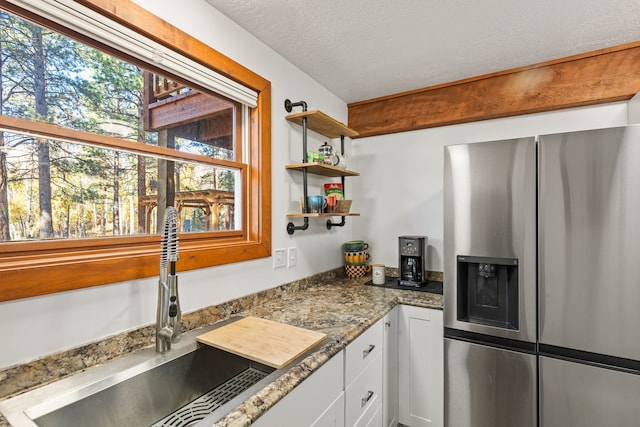 kitchen featuring white cabinetry, sink, stainless steel refrigerator with ice dispenser, dark stone counters, and a textured ceiling