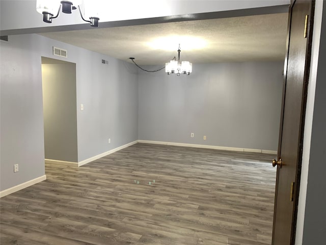 empty room with a textured ceiling, dark hardwood / wood-style floors, and an inviting chandelier