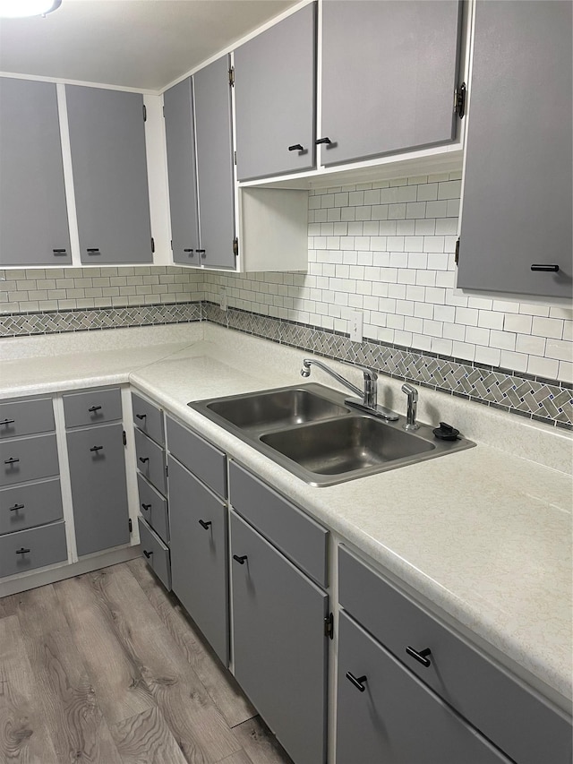 kitchen with gray cabinetry, decorative backsplash, light hardwood / wood-style floors, and sink