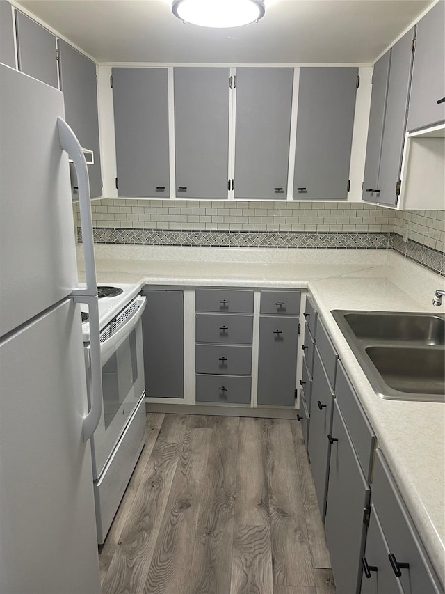 kitchen featuring sink, dark hardwood / wood-style flooring, backsplash, white appliances, and gray cabinets