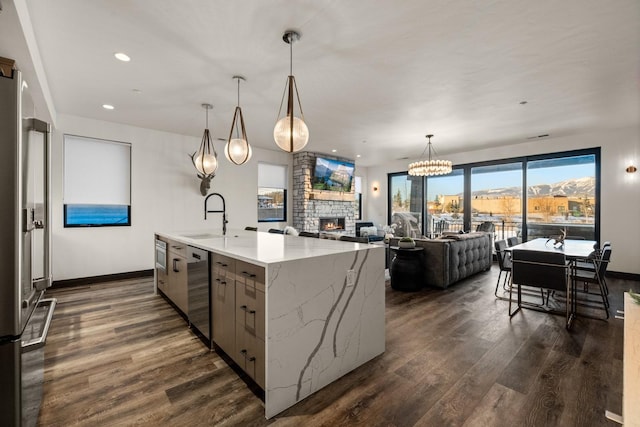 kitchen with a kitchen island with sink, sink, a fireplace, light stone counters, and stainless steel appliances