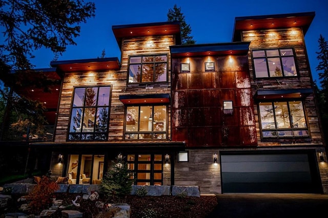1148 Glades Dr, Whitefish, MT 59937 - back of house at night featuring a balcony, an attached garage, and driveway