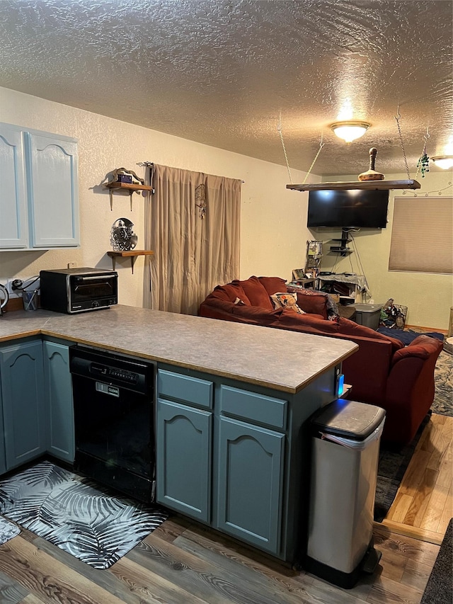 kitchen featuring black dishwasher, blue cabinets, kitchen peninsula, hardwood / wood-style floors, and a textured ceiling