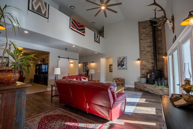 living room featuring a towering ceiling, a wood stove, ceiling fan, and dark wood-type flooring