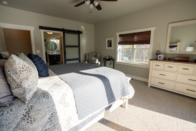 bedroom with ensuite bathroom, a barn door, carpet floors, and ceiling fan